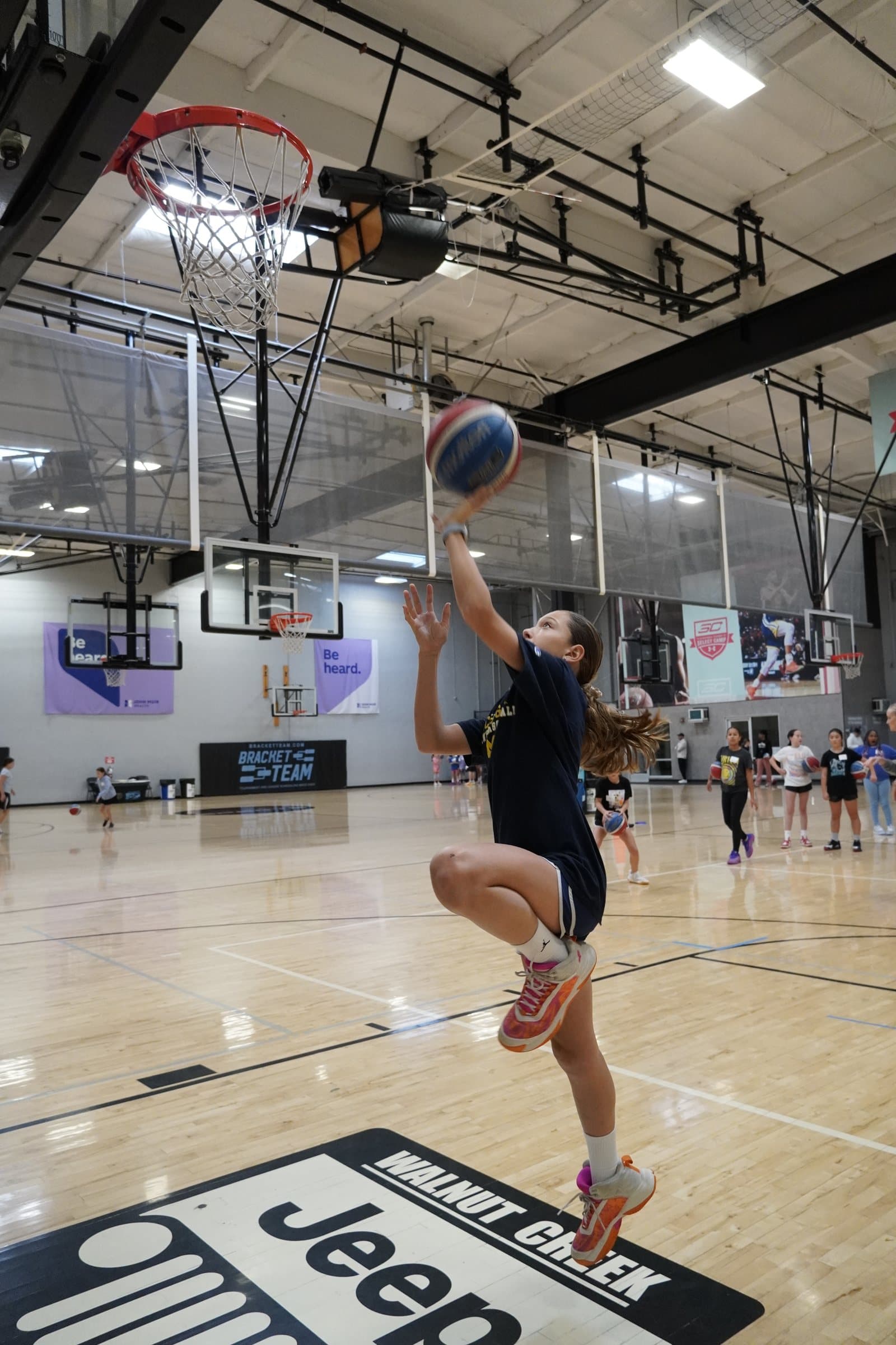A player rises for a layup at an ISI all-girls basketball clinic while teammates watch.