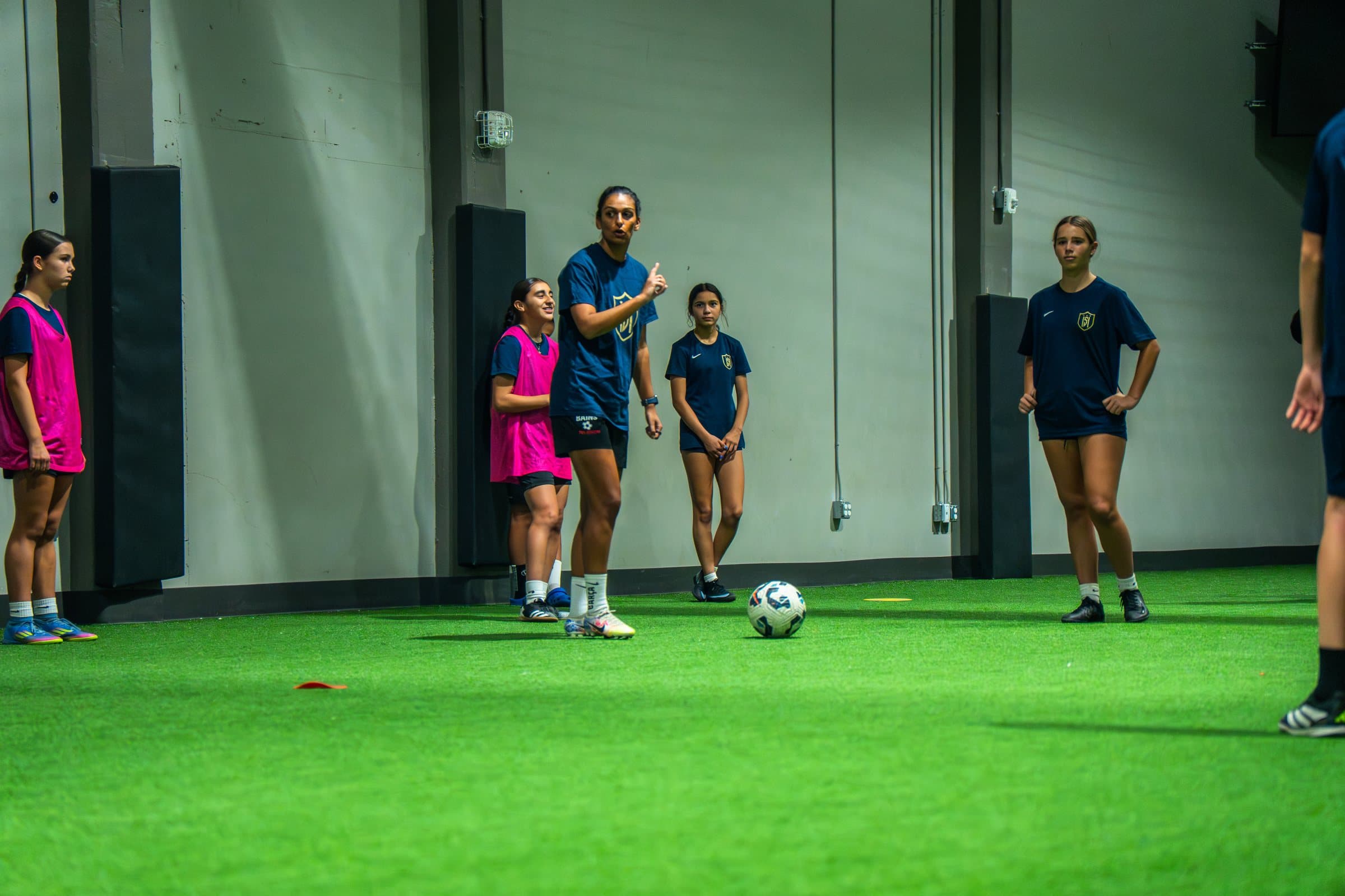 A coach demonstrating a move to a group of soccer players on an indoor pitch.